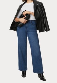 Breda blå denimjeans med midja, kombinerade med en svart skinnjacka och en svart clutchtväska, med släta texturer.