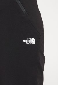 Svarta träningsbyxor med en sidodragkedjeficka och en vit logotyp från The North Face på låret. Slät yta, strömlinjeformat design.