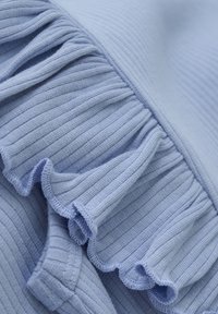 Hellblau gestreifter Stoff mit einem Rüschensaum. Die Textur ist weich, mit einem dezenten Glanz, der die Rillen und Kanten der Rüsche betont.