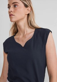 Top a coste blu navy con scollatura a V e maniche corte. Il tessuto ha una superficie liscia, che mette in risalto il design aderente.