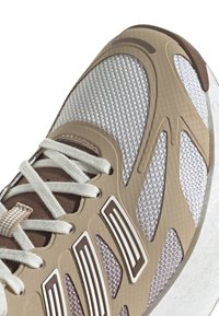 Bež sportska cipela s prozračnom mrežastom gornjom snagom, gumiranim detaljima i istaknutim izrezima. Uključene su vezice i podstavljeni ovratnik.