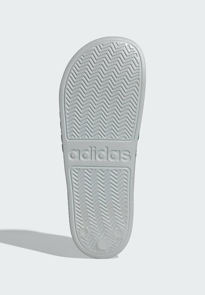 Hvid gummisål med zigzag mønster og indgraveret "adidas" logo. Glat overflade med afrundede kanter.