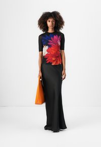 Zwarte, aansluitende rok gecombineerd met een top met korte mouwen en een kleurrijk bloemmotief. Het model houdt een felle oranje schoudertas vast.