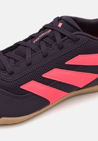 Dunkellila Sportschuh mit atmungsaktivem Mesh, pinken Akzenten und drei markanten Streifen. Die Sohle ist hellbraun und flach, um Stabilität zu gewährleisten.
