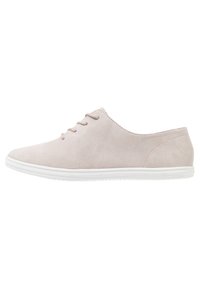 Zapato de ante rosa claro con punta redondeada, minimalista en su cordonera y con suela de goma blanca. Textura suave y diseño sencillo.