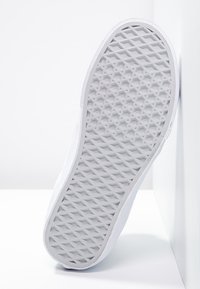 White sneaker with a textured rubber sole featuring a diamond pattern, smooth sides, and a minimalistic design.