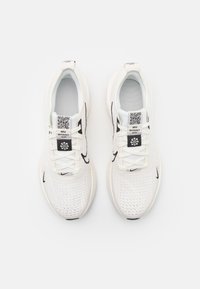 Baskets de sport blanches avec un dessus en maille, accents noirs, une étiquette avec un code QR et une semelle texturée. Lacets et un col rembourré inclus.