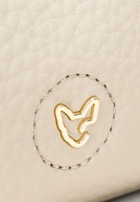 Pelle color crema con logo di volpe in tonalità oro, contornato da un motivo circolare cucito in filo di contrasto.