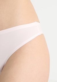 Light pink sheer thong made of smooth, lightweight fabric. Features a thin waistband with minimal coverage and a seamless design.