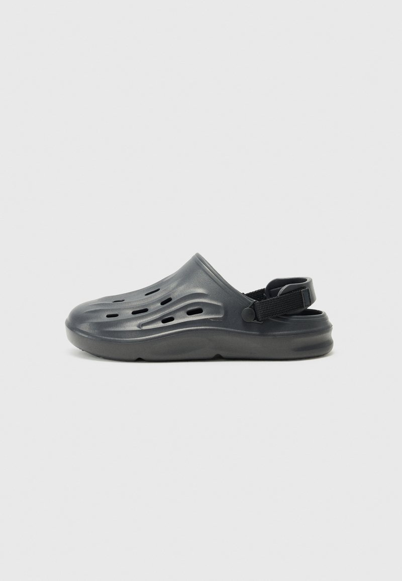 Black molded plastic clogs with ventilation holes and a rear strap, featuring a smooth surface and rounded shape for comfort.