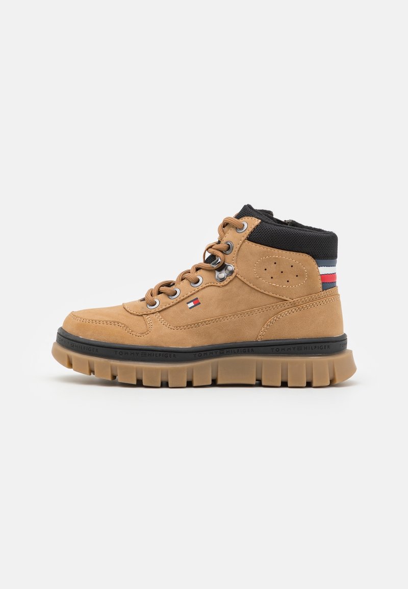 Baskets montantes beige avec semelle robuste, œillets métalliques, col rembourré noir et bandes rouges, blanches et bleues au talon et logo latéral.
