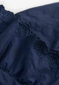 Tessuto blu navy con bordi ondulati e ricami floreali. Morbida consistenza con una leggera lucentezza, che mette in risalto i dettagli e l'artigianato di alta qualità.