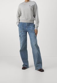 Felpa grigia con collo a giro e piccolo dettaglio grafico; abbinata a jeans cargo a gamba larga blu chiaro con più tasche.