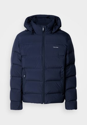 Giacca puffer blu navy con cappuccio, dotata di zip completa, due tasche laterali e pannelli cuciti per l'isolamento. Logo sottile sul petto.
