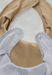 Två tygsalar, en beige och en ljusgrå, med tryckknappar och mjukt textilt material. Varje har en slät, rundad form.
