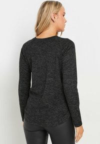 Zwarte lange mouwen shirt in een zachte, gestructureerde stof met een afgeronde onderrand, met raglanmouwen en een ontspannen pasvorm.
