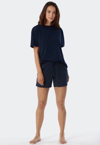 Marinblå bomulls-t-shirt med kort ärm, matchad med marinblå shorts som har ett mönster av vita prickar och dragsko i midjan.