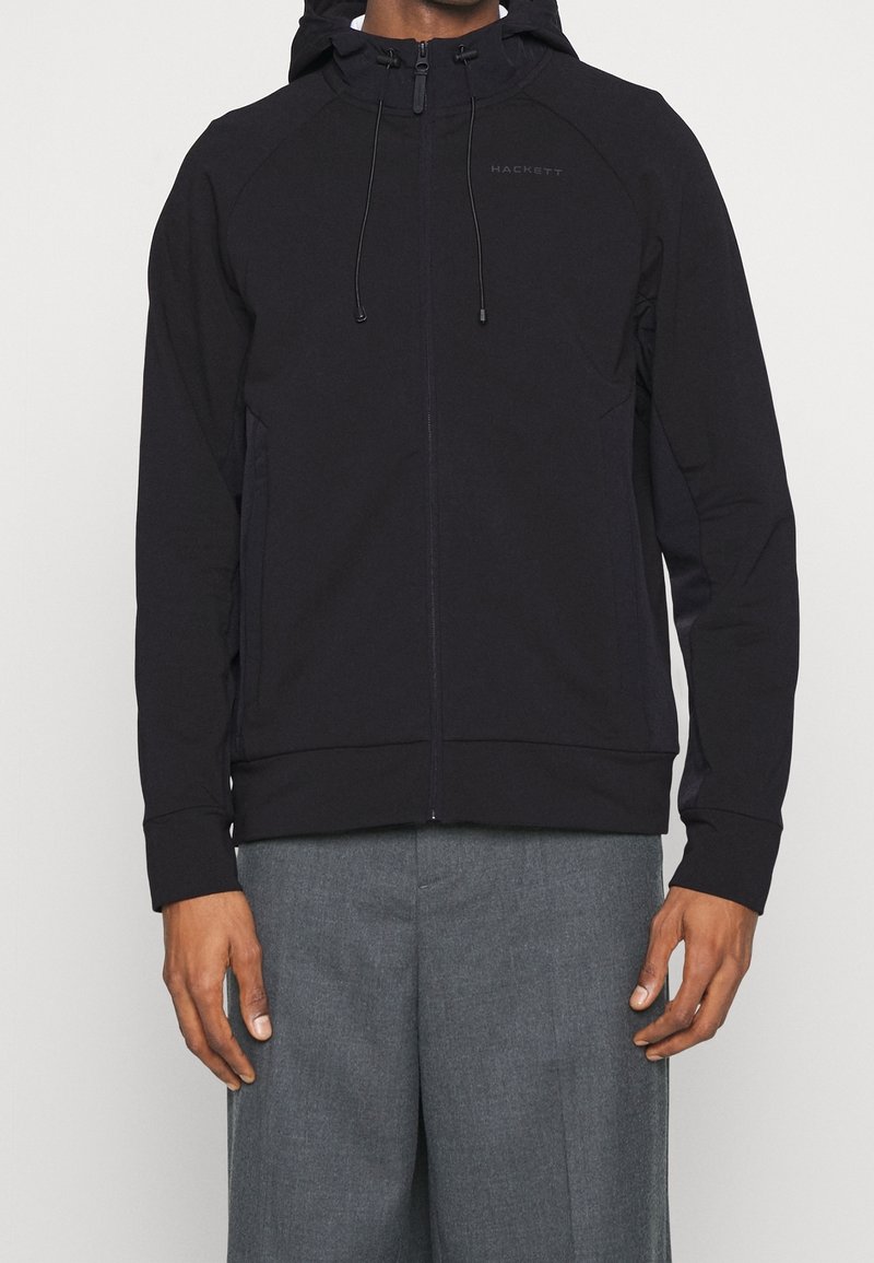 Giacca con cappuccio nera e zip completa, cappuccio con cordino e maniche raglan. Presenta un design aderente e una texture di tessuto morbido.