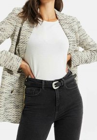 Lätt texturerad kavaj i kräm och svart över en vit topp, kombinerad med högmidjade svarta jeans och ett flätat svart bälte med silverfäste.