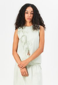 Top senza maniche verde chiaro con lacci decorativi lungo il lato sinistro e un design leggermente cropped, realizzato in un tessuto morbido e liscio.