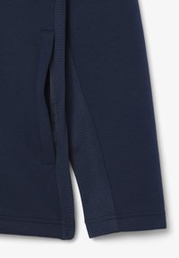 Close-up of navy blue garment sleeve with side pocket and textured fabric panel along the side seam.