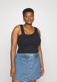 Top cropped preto sem mangas com alças largas, combinado com uma saia de ganga azul clara com botões à frente, apresentando dois bolsos frontais.