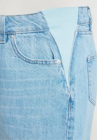 Vaqueros de mezclilla azul claro con una cinturilla elástica, que cuentan con bolsillos frontales y un cierre de botón visible. Tejido suave y texturizado.