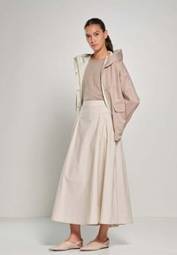 Lichte, beige ritsjack over een taupe top, gecombineerd met een vloeiende, crèmekleurige maxi-jurk en nude slingback schoenen. Minimalistisch ontwerp.