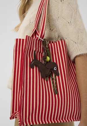 Rote und beige gestreifte Canvas-Tragetasche mit langen Griffen, versehen mit einem schlüsselanhänger in Form eines braunen Hundes, der an einem grünen Band befestigt ist.