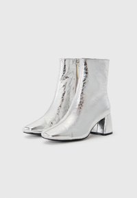Silberne Stiefeletten mit glänzendem Metallic-Finish, spitzem Zeh und mittelhohem Blockabsatz sowie einem seitlichen Reißverschluss für einfaches An- und Ausziehen.