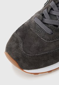 Gray suede sneaker featuring textured surface, rounded toe, contrasting gray laces, and a rubber sole with brown accents.