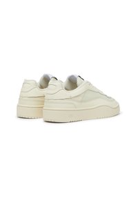 Cream-colored sneakers made of leather and mesh, featuring a chunky rubber sole with a textured grip pattern and minimalist design elements.