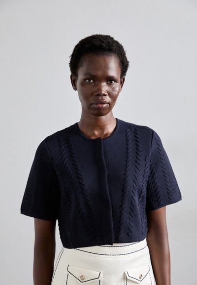 Top court en maille navy avec des motifs texturés et des manches courtes, associé à une jupe blanche dotée de deux poches avant et de coutures contrastantes.