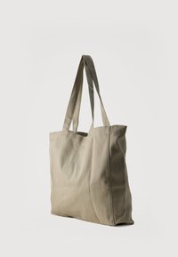 Μπεζ τσάντα ώμου από ύφασμα με δύο ιμάντες, όρθια σε απλό λευκό φόντο.