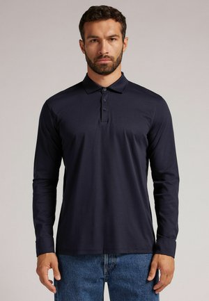 Long-sleeve polo shirt in navy, featuring a classic collar and four-button placket. Soft fabric with a smooth texture, paired with denim jeans.