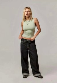 Top de alças ajustado em verde claro, combinado com jeans de perna larga de denim escuro de cintura alta. Os jeans apresentam um cordão e bainhas dobradas.