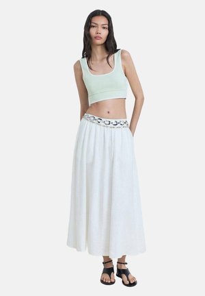 Light green cropped tank top, white maxi skirt with a textured, elastic waistband, accented with a metallic belt, paired with black sandals.