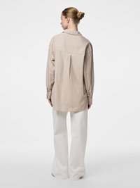 Smėlio spalvos dryžuota marškinėliai su nugara klostė, apykakle ir ilgomis rankovėmis, derinami su plačiomis baltomis kelnėmis iš lengvos medžiagos.