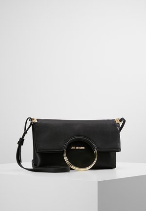 Sac à bandoulière noir Love Moschino avec anneau circulaire doré et bandoulière réglable sur une surface blanche avec un fond uni.