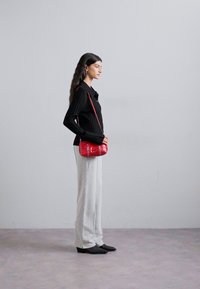 Rote Leder-Umhängetasche mit runder Form, versehen mit einem kleinen Deckel, kunstvollen Nähten und einem dünnen Schultergurt.