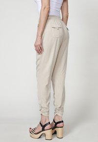 Beige jogger-housut, joissa on elastinen vyötärö, lahkeet käännettyinä ja sivutaskut. Yhdistetty mustavalkoisiin kuvioituihin korkokenkiin.