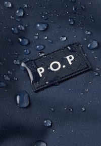 Waterdruppels op donkerblauwe stof met een rechthoekig label "P.O.P", die de waterbestendige textuur en duurzaamheid van het materiaal benadrukken.