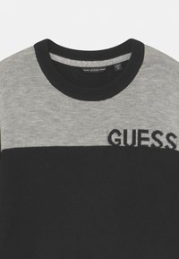 Maglione a girocollo nero e grigio con un design a blocchi di colore orizzontali, caratterizzato dalla scritta "GUESS" in nero in contrasto, lavorata sul petto.