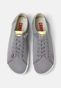 Gray canvas sneakers with round toe, white rubber sole, six eyelets, and a yellow and red branded insole. Classic lace-up design.