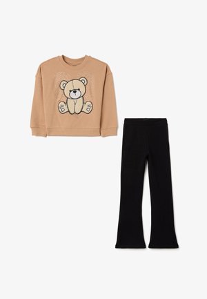 Lichtbruine sweatshirt met een teddybeerafbeelding en strassaccenten, gecombineerd met zwarte flared leggings. Zachte, casual stof.
