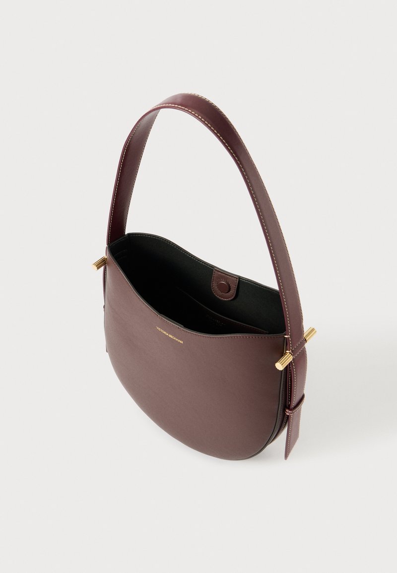 Bordeaux leren handtas met ronde vorm, gouden hardware accenten en een contrasterende zwarte binnenkant. Voorzien van een enkele schouderband.