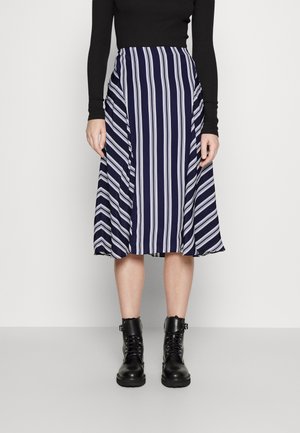 Et marineblå og hvit stripete midi-skjørt med en flytende design, kombinert med svarte snøresko av kampstil. Glatt stoff med en svak glans.