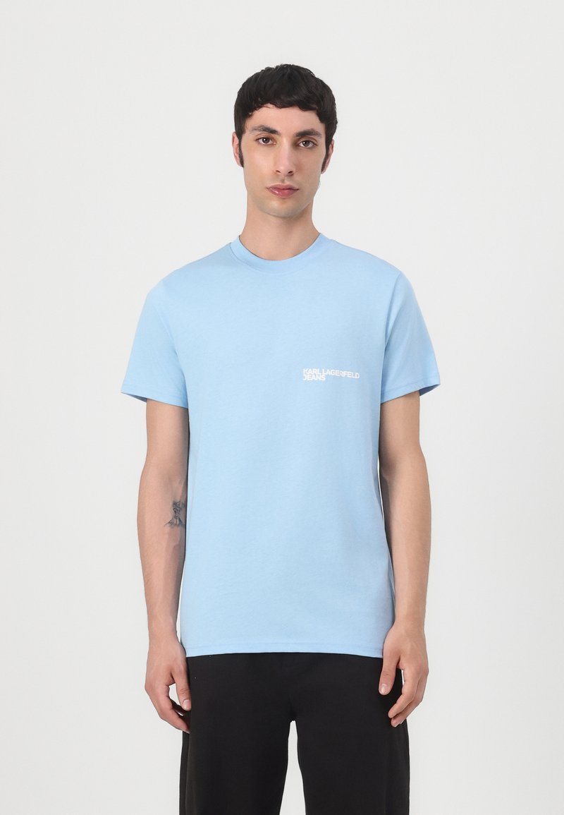 T-shirt en coton bleu clair avec col rond et manches courtes, avec un logo blanc imprimé sur la zone du poche gauche.