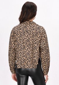 Cămașă bej cu imprimeu leopard negru, dintr-un material texturat, cu mâneci lungi și croială lejeră, asortată cu leggings negri.