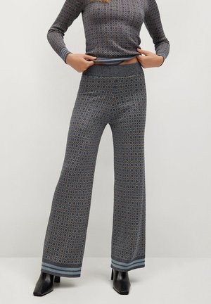 Femme portant un haut à manches longues à motif assorti et un pantalon à jambes larges avec des poignets rayés bleus, assortis à des bottines noires à talons.